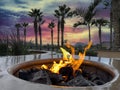 Glowing natural gas fire pit plus ceramic rocks with palm trees with sunset Royalty Free Stock Photo