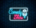 Glowing neon comedy show sign with retro microphone in rectangle frame on a brick wall background.