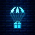 Glowing neon Gift box flying on parachute icon isolated on brick wall background. Delivery service, air shipping concept Royalty Free Stock Photo