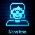 Glowing neon Hacker or coder icon isolated on brick wall background. Programmer developer working on code, coding