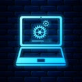 Glowing neon Laptop and gears icon isolated on brick wall background. Laptop service concept. Adjusting app, setting Royalty Free Stock Photo