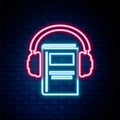 Glowing neon line Audio book icon isolated on brick wall background. Book with headphones. Audio guide sign. Online Royalty Free Stock Photo