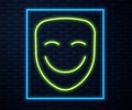 Glowing neon line Comedy theatrical mask icon isolated on brick wall background. Vector