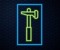 Glowing neon line Hammer icon isolated on brick wall background. Tool for repair. Vector