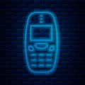 Glowing neon line Old vintage keypad mobile phone icon isolated on brick wall background. Retro cellphone device Royalty Free Stock Photo