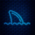 Glowing neon line Shark fin in ocean wave icon isolated on brick wall background. Vector
