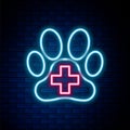 Glowing neon line Veterinary clinic symbol icon isolated on brick wall background. Cross hospital sign. A stylized paw