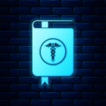 Glowing neon Medical book and Caduceus medical symbol icon isolated on brick wall background. Medical reference book