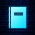 Glowing neon Notebook icon isolated on brick wall background. Spiral notepad icon. School notebook. Writing pad. Diary