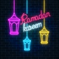 Glowing neon ramadan holy month sign on dark brick wall background. Ramadan greeting card with fanus lanterns. Royalty Free Stock Photo