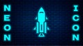 Glowing neon Rocket ship with fire icon isolated on brick wall background. Space travel. Vector
