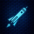 Glowing neon Rocket ship with fire icon on brick wall background. Space travel. Vector
