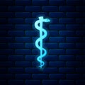 Glowing neon Rod of asclepius snake coiled up silhouette icon isolated on brick wall background. Emblem for drugstore or