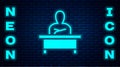 Glowing neon Schoolboy sitting at desk icon isolated on brick wall background. Vector