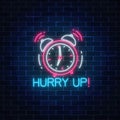 Glowing neon sign with alarm clock and hurry up text on dark brick wall background. Call to action symbol Royalty Free Stock Photo