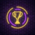 Glowing neon sign with award cup in round frame on dark brick wall background. Winner cup honorary trophy