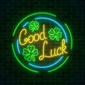 Glowing neon sign with geed luck wish and four-leaf clovers in circle frames on dark brick wall background. Royalty Free Stock Photo