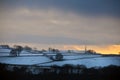 Glowing orange sunset in a cloudy twilight winter sky with snow covered fields with stoodley pike monument in the distance in