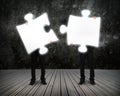 Glowing puzzles businessmen hold to connect illuminating dark wooden floor Royalty Free Stock Photo