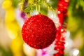Glowing red Christmas ball and colorful shining tinsel hanging on branch of tree. Close-up view Xmas festive composition Royalty Free Stock Photo
