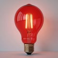Glowing red lightbulb in center with golden stem, soft warm light on cool grey background. Vibrant scene with single light Royalty Free Stock Photo