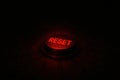 Bright Red Reset Button Illuminated in Darkness on a Textured Surface Ready for Action Royalty Free Stock Photo