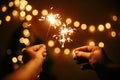 Glowing sparklers in hands on background of golden christmas tree lights, couple celebrating in dark festive room. Happy New Year Royalty Free Stock Photo