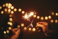 Glowing sparklers in hands on background of golden christmas tree lights, couple celebrating in dark festive room. Happy New Year Royalty Free Stock Photo