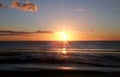 Sunset with lens flare over a calm blue sea and beach with illuminated orange clouds Royalty Free Stock Photo