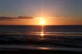 Glowing sunset with lens flare over a calm blue sea and beach with illuminated orange clouds Royalty Free Stock Photo