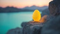 Glowing yellow egg shaped object rests on a rocky cliff overlooking a serene lake at sunset Royalty Free Stock Photo
