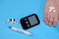 Glucometer and hand with pills on a blue background.