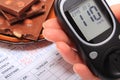 Glucometer in hand and portion of chocolate on medical form