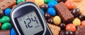 Glucometer with result of sugar level and candies with cookies. Diabetes and reduction of eating sweets