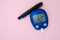 Glucometer with test strip and lancelet on pink background. Diabetes, gestational diabetes mellitus concept.