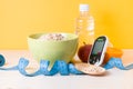 glucose meter, bottle of water, fruits, a bowl of oatmeal and a blue measuring tape on the table, yellow background Royalty Free Stock Photo