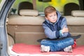 Glum little boy sitting in the boot of a car.