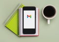 Gmail logo on black screen of smartphone with notebooks and cup of coffee