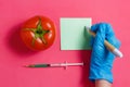 GMO Scientist Make Note, Green Liquid in Syringe,Red Tomato - Genetically Modified Food Concept on Pink Background.