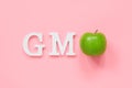 GMO tex from white volume letters and green apple on pink background. Concept of genetically modified foods or fruits. Top view Royalty Free Stock Photo