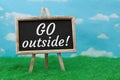 Go Outside message on standing chalkboard on grass with sky