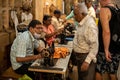 Goa, India, February 2023. Side view of Indian man tailor in disposable mask sit at sewing machine, talk to senior man.