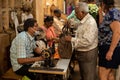 Goa, India, February 2023. Side view of middle-aged Indian man tailor sitting at sewing machine, talking to senior man.