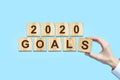 2020. Goals. Female hand makes up words from wooden blocks. Isolated on a blue background. New Year Goals Concept. Royalty Free Stock Photo