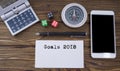 Goals 2018 written on paper, wooden background desk with calculator, dice, compass, smart phone and pen.