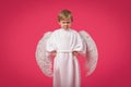 God Angel gets angry and punishes with glance. Child boy kid in suit with wings on pink background. Concept of sins and holidays