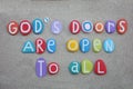 God\'s doors are open to all, creative text composed with multi colored stone letters over beach sand