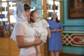 Godmother with goddaughter stand in the Orthodox church. Mother standing on the side. Ceremony of sacrament of initiation into the