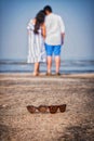 Goggles in focus with couple standing in the background on the beach