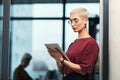 Going through company emails. an attractive young businesswoman wearing spectacles and using a tablet while standing Royalty Free Stock Photo